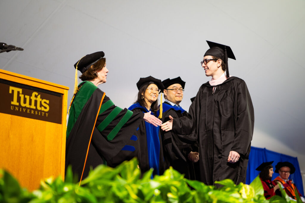 Tufts University School of Medicine Commencement attendees shake hands on stage.